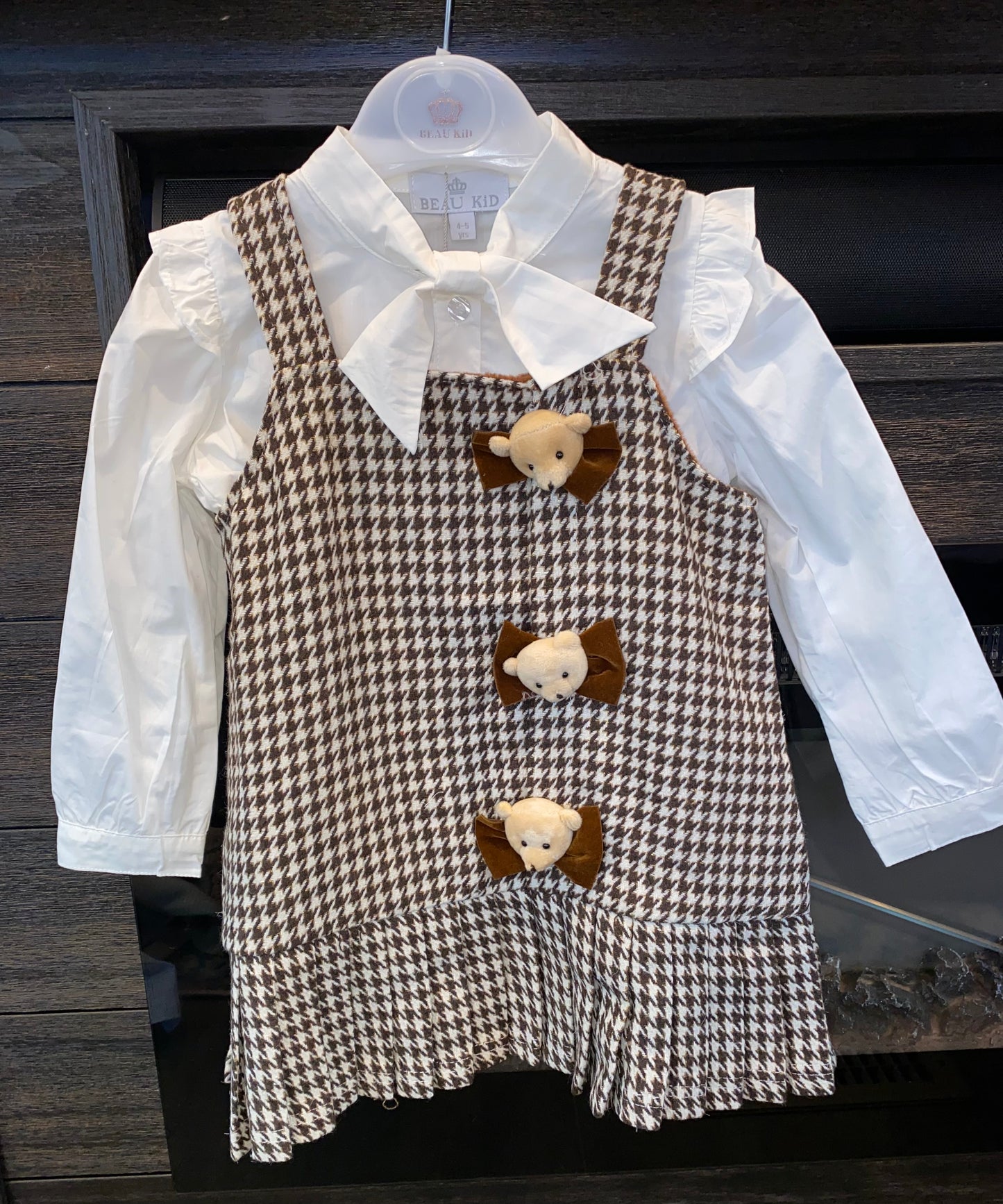 Children's outfit with houndstooth pattern dress over a white shirt on a wooden surface.