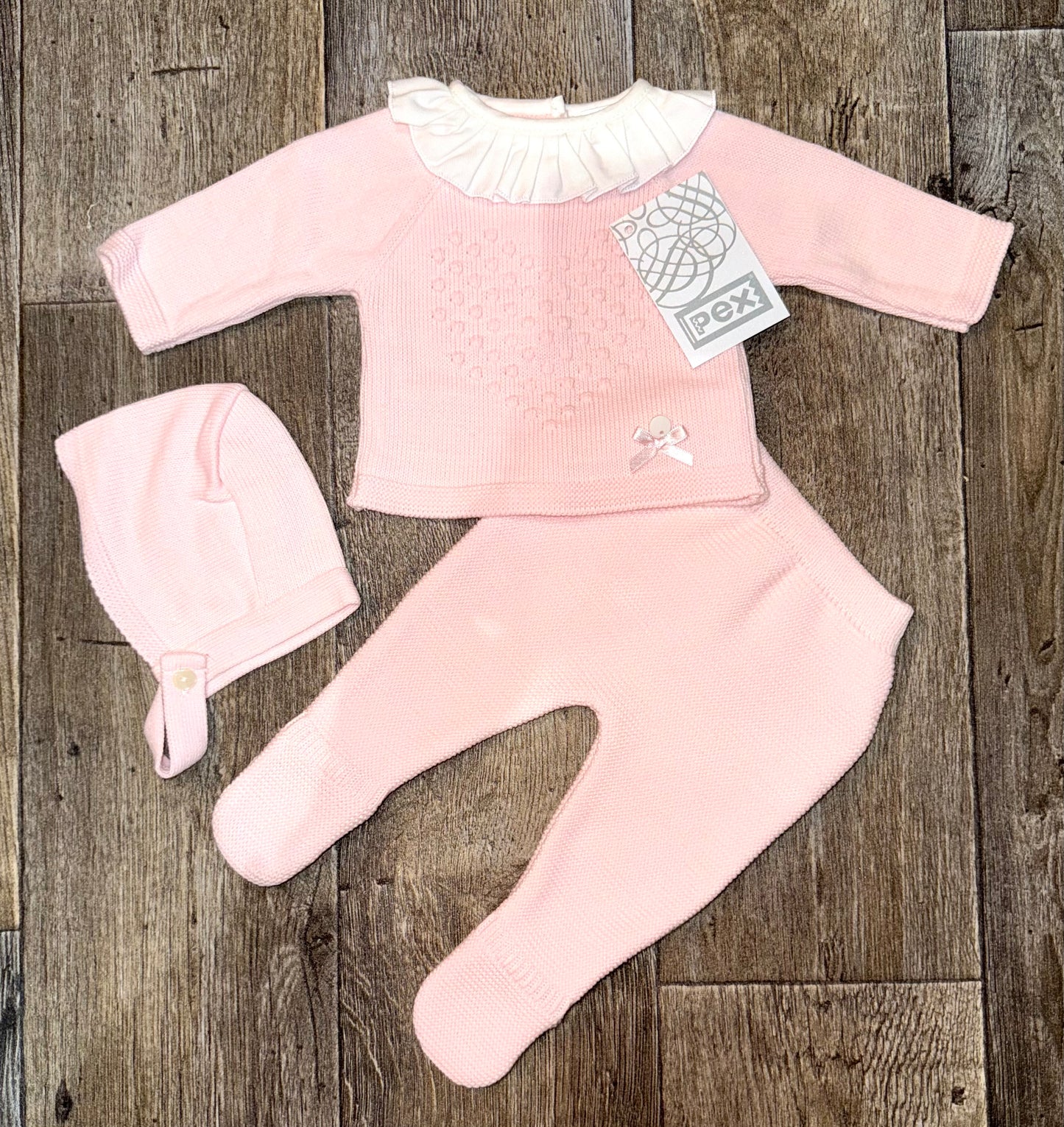 Pink baby outfit with matching hat on a wooden surface