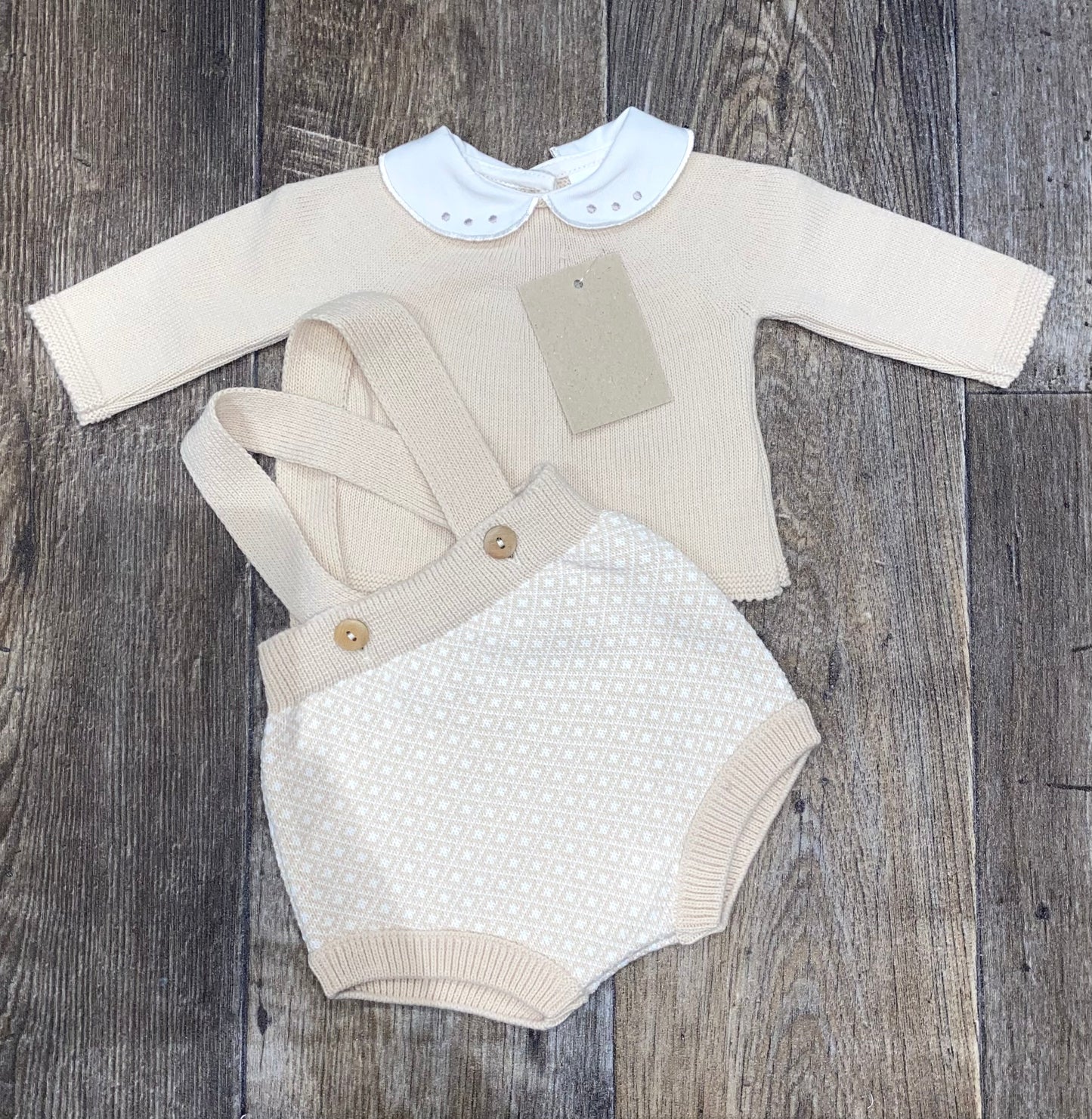Baby outfit with beige long-sleeve top and white textured pants on a wooden surface