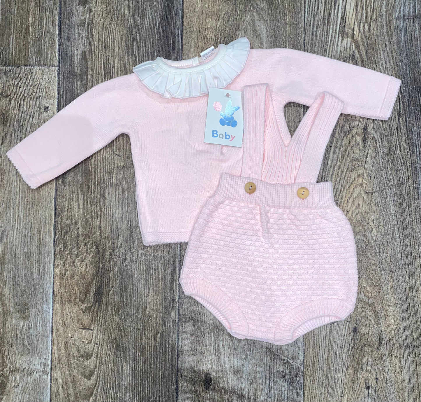Baby outfit with pink long-sleeve top and knitted romper on a wooden surface