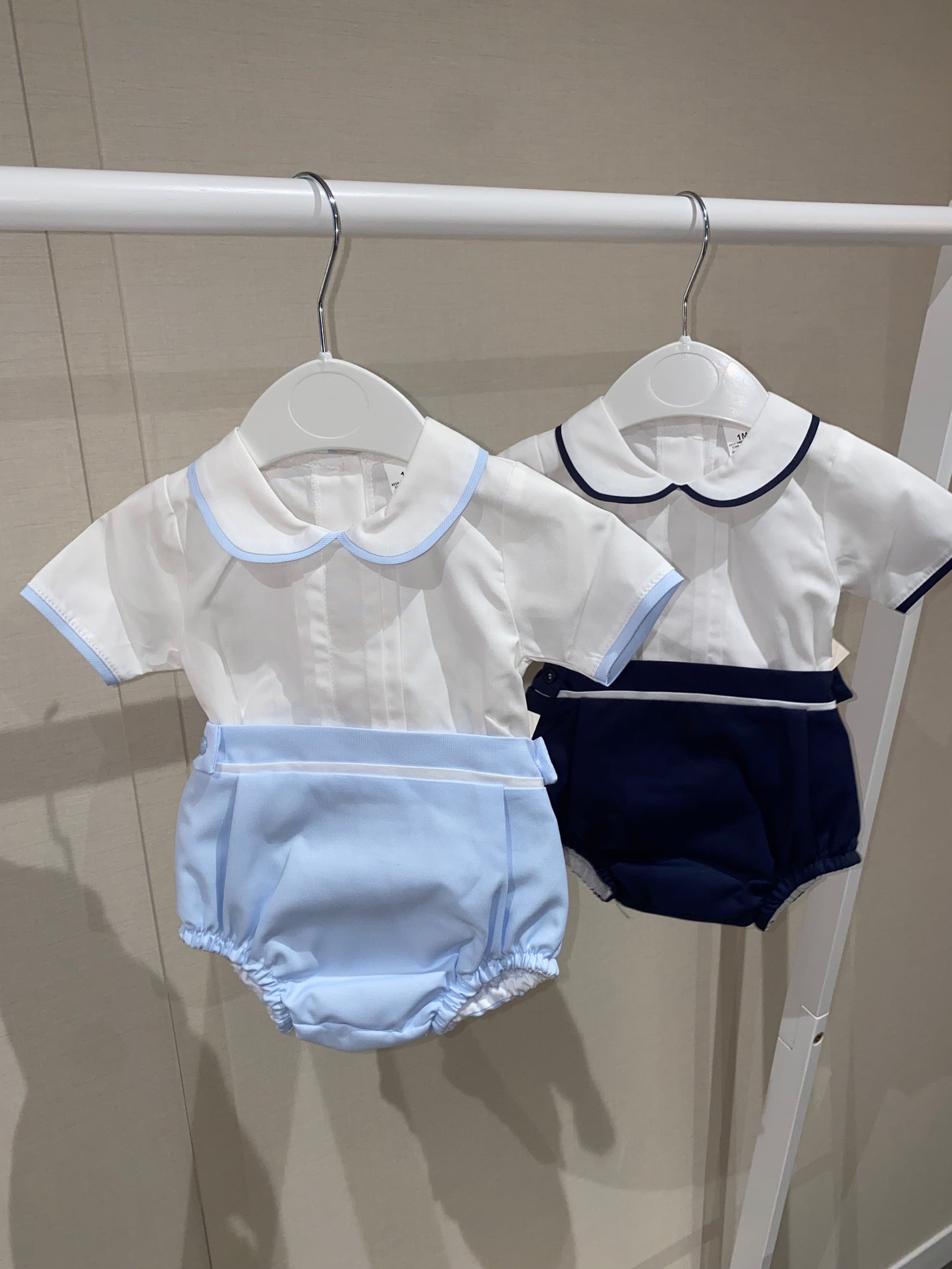 Children's clothing including a white top, navy shorts, and light blue bloomers hanging on a clothesline.