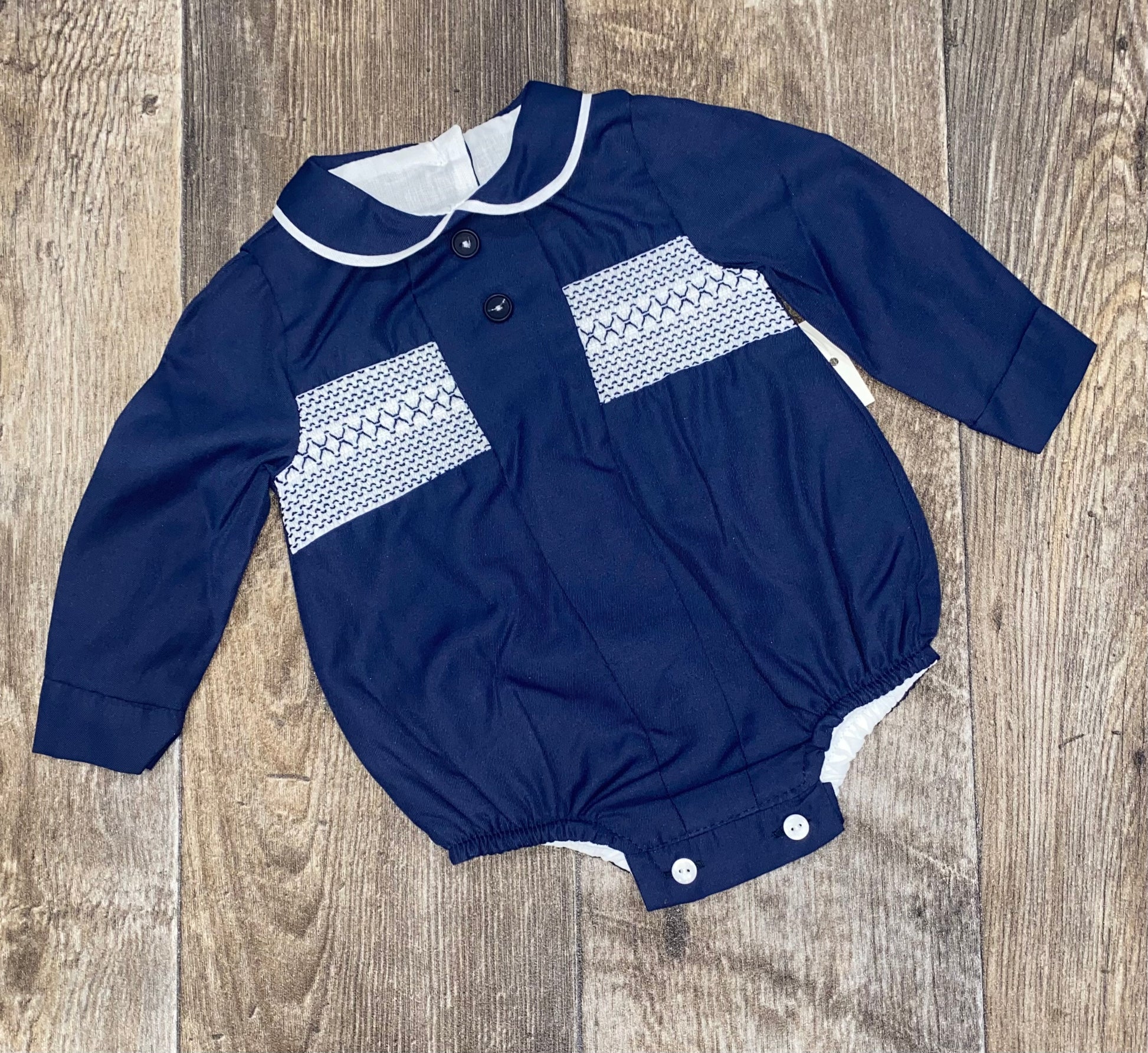 Navy blue baby romper with white pattern smock detail on a wooden surface