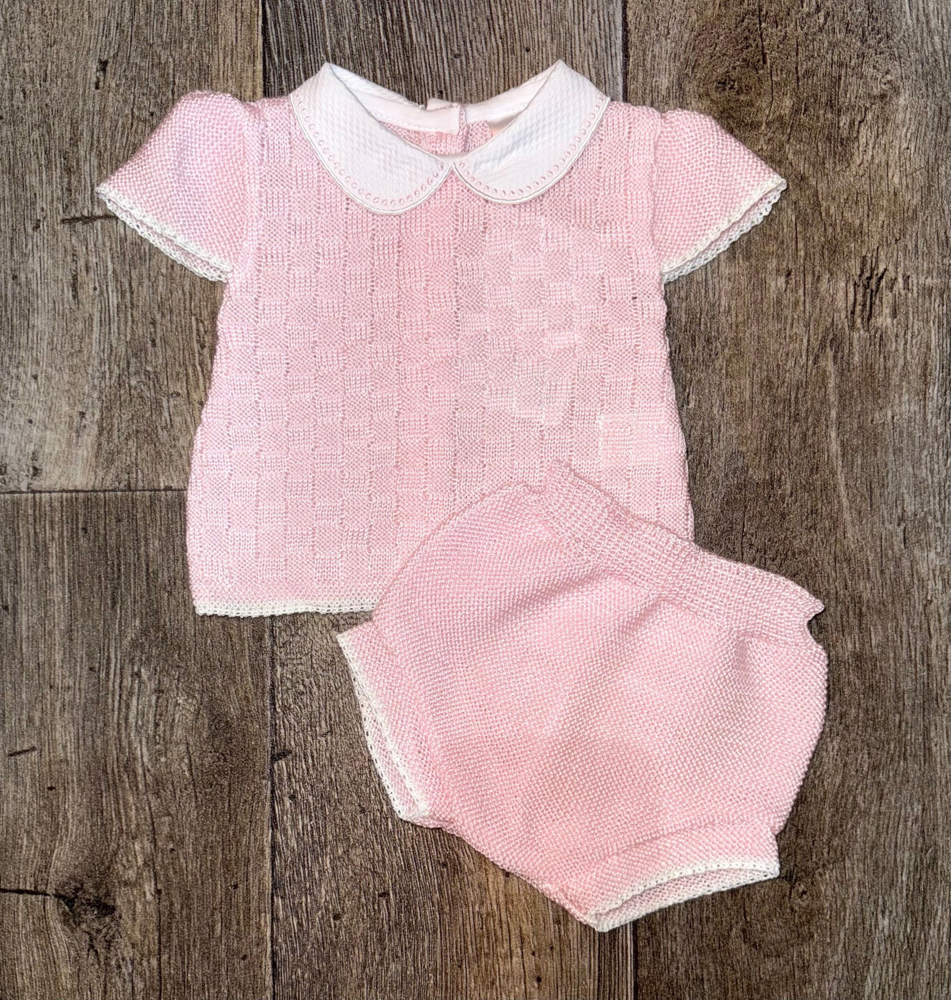 Pink knitted outfit with white collar on a wooden surface