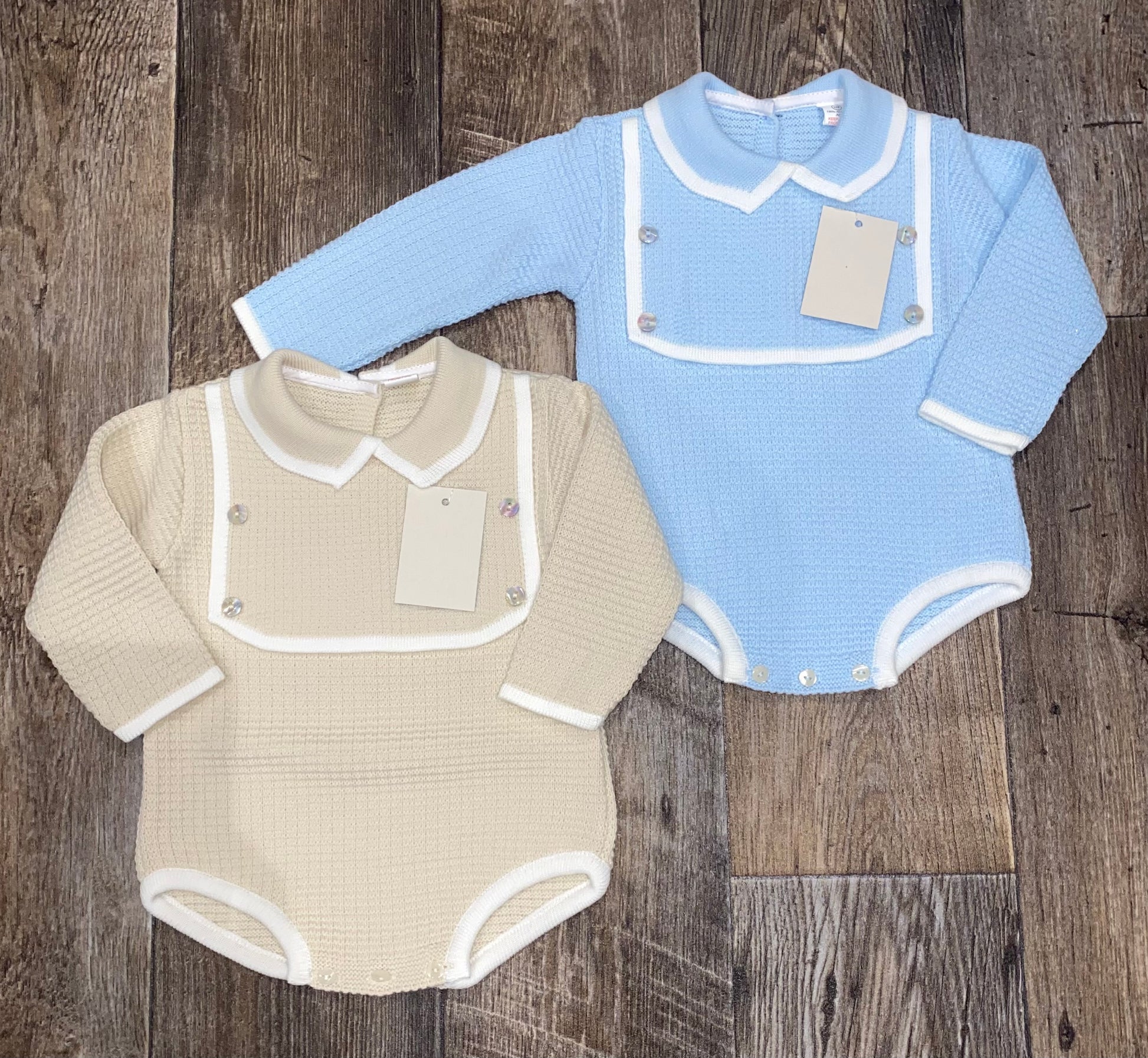 Two baby rompers, one beige and one blue, on a wooden surface.