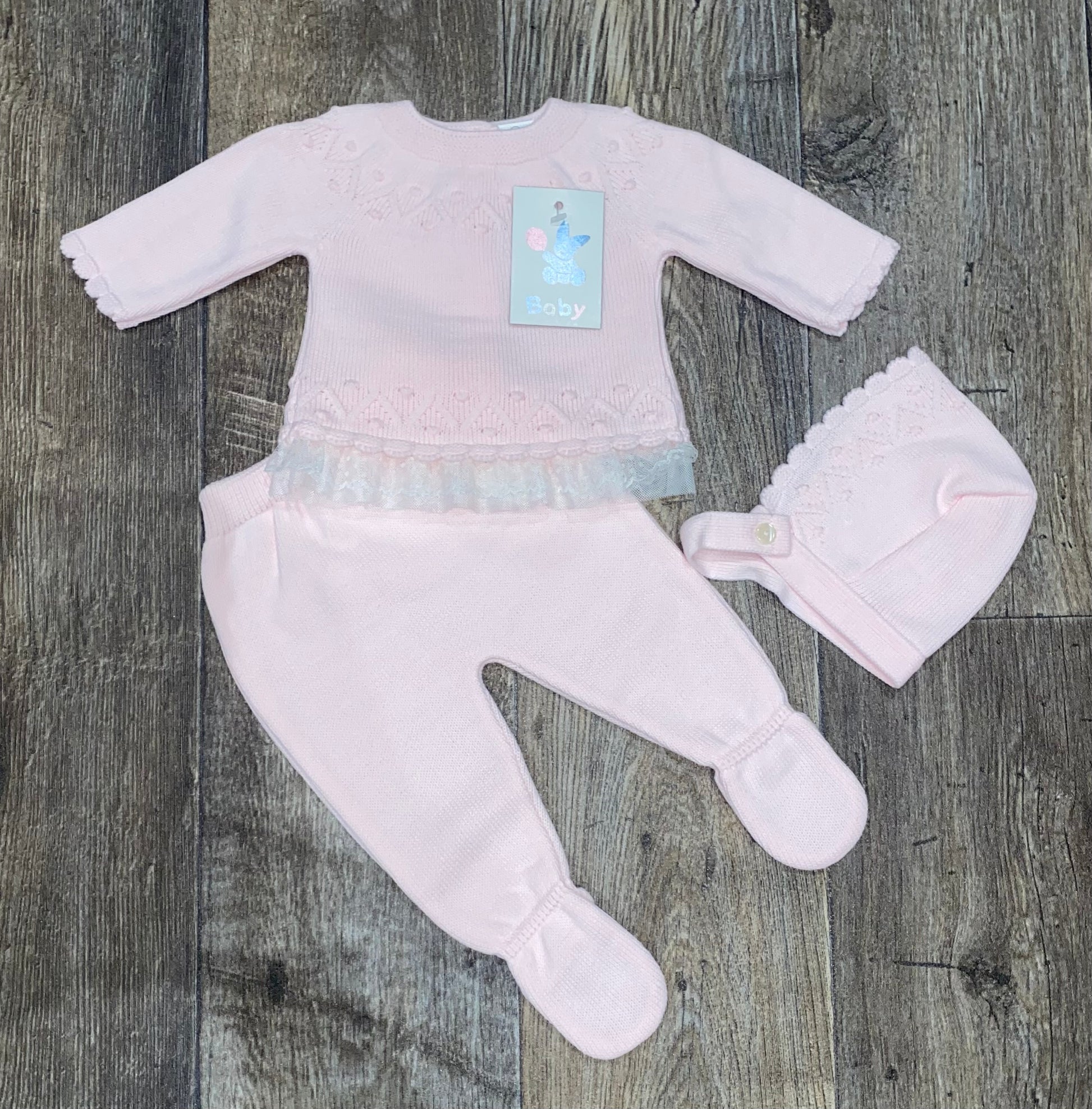 Baby outfit set with white top, pants, and hat on a wooden surface