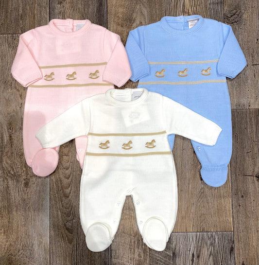 Three baby rompers in pink, white, and blue on a wooden surface.