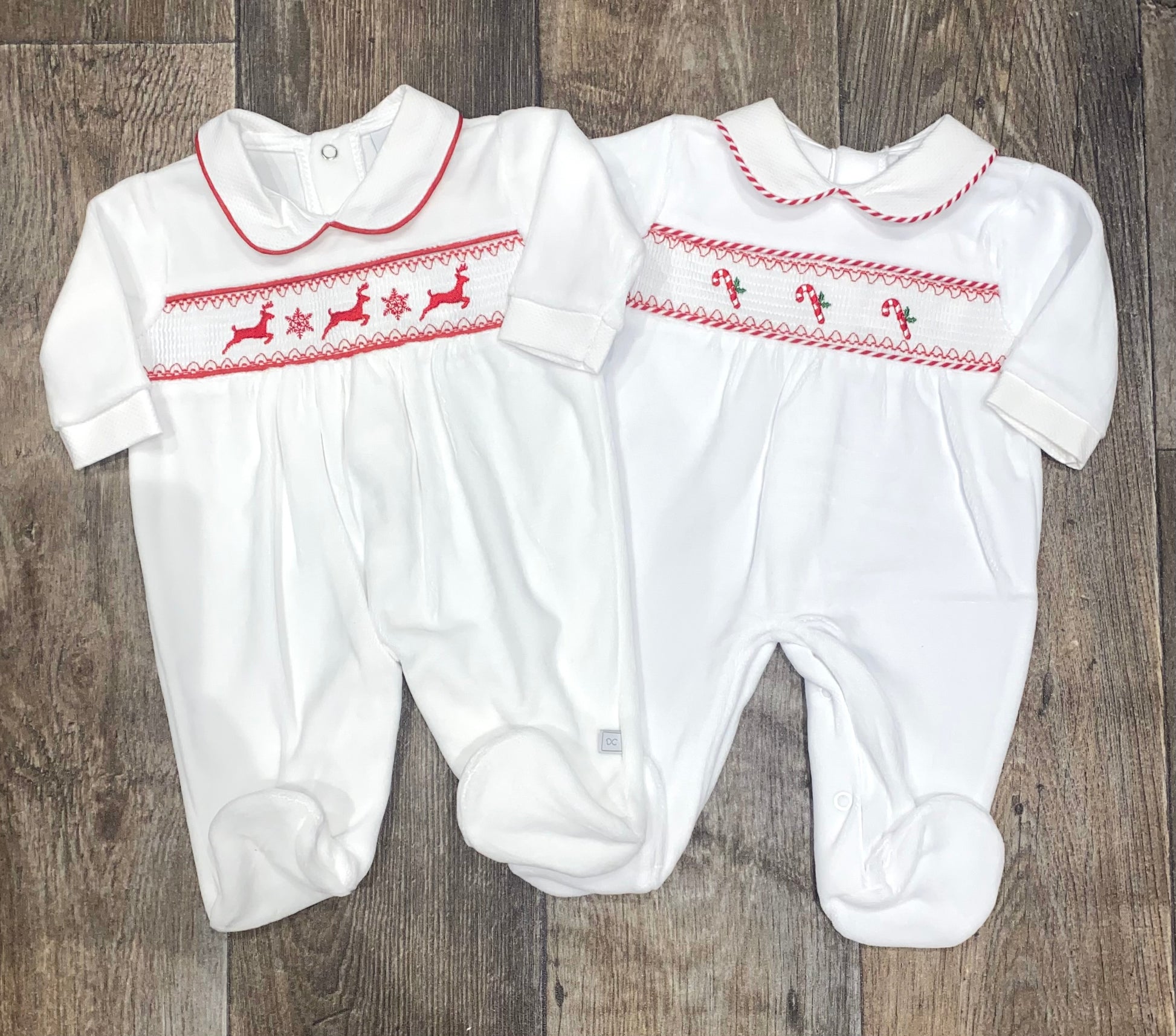 Two white baby rompers with red Christmas themed embroidery on a wooden surface