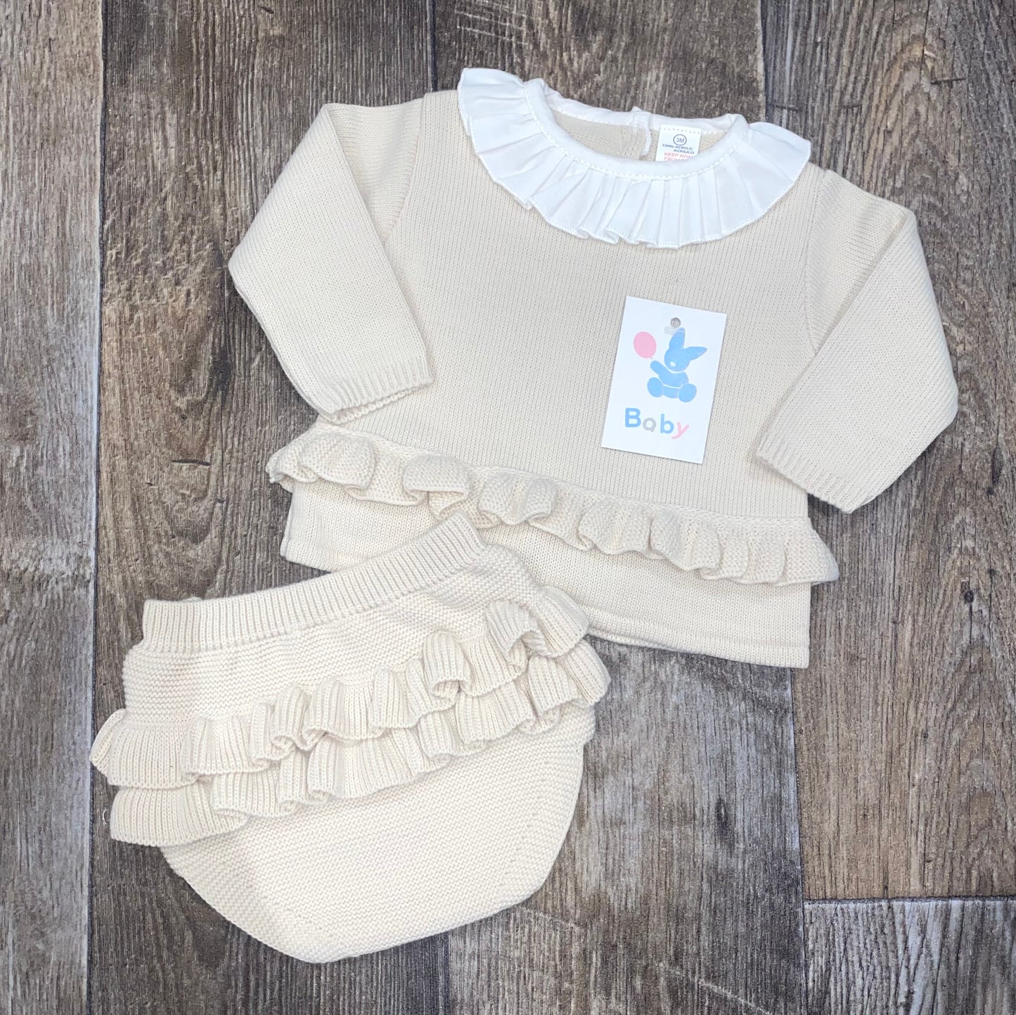 Baby outfit with ruffled top and bloomers on a wooden surface