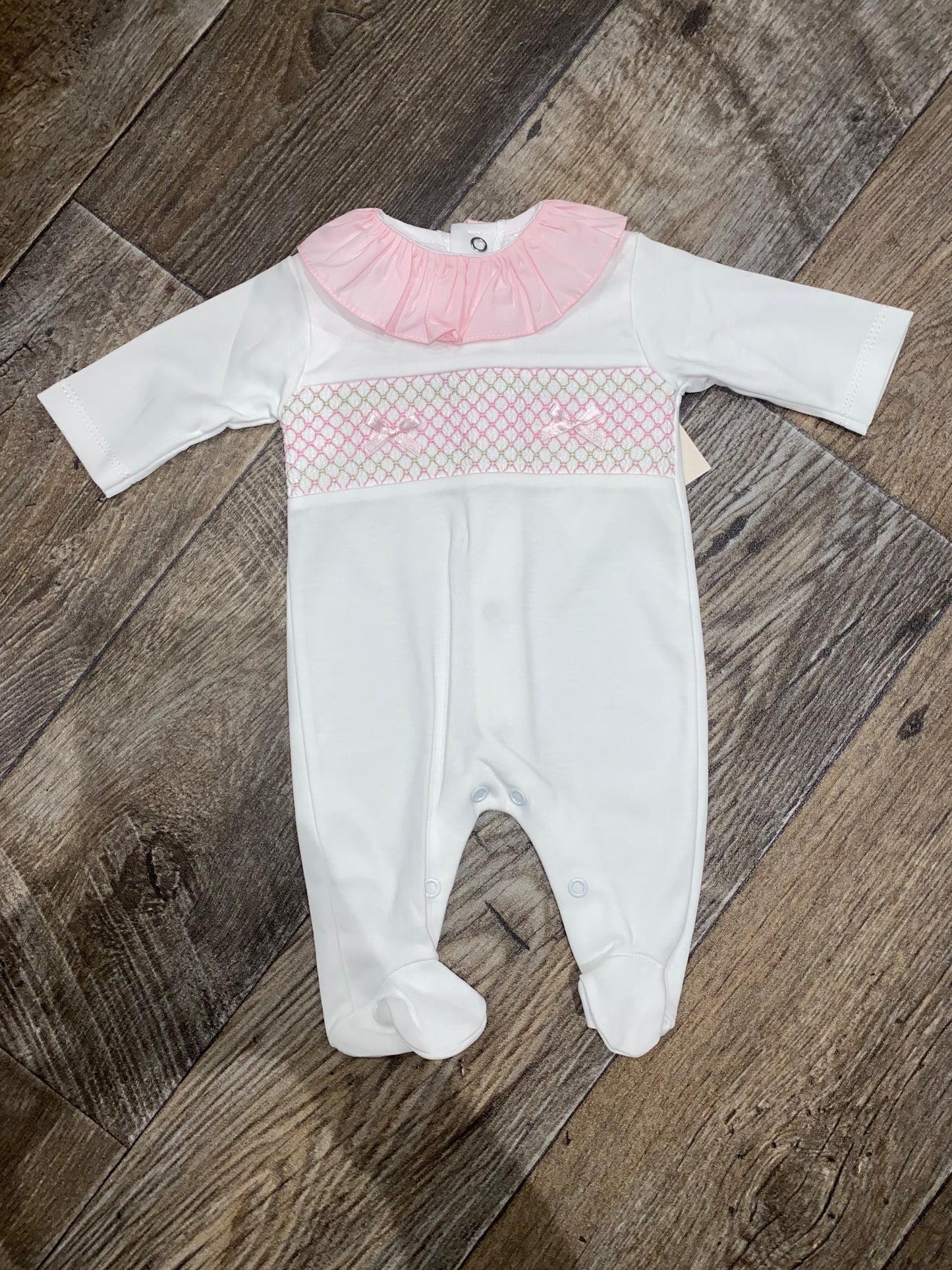 White baby outfit with pink smocking details on a wooden floor