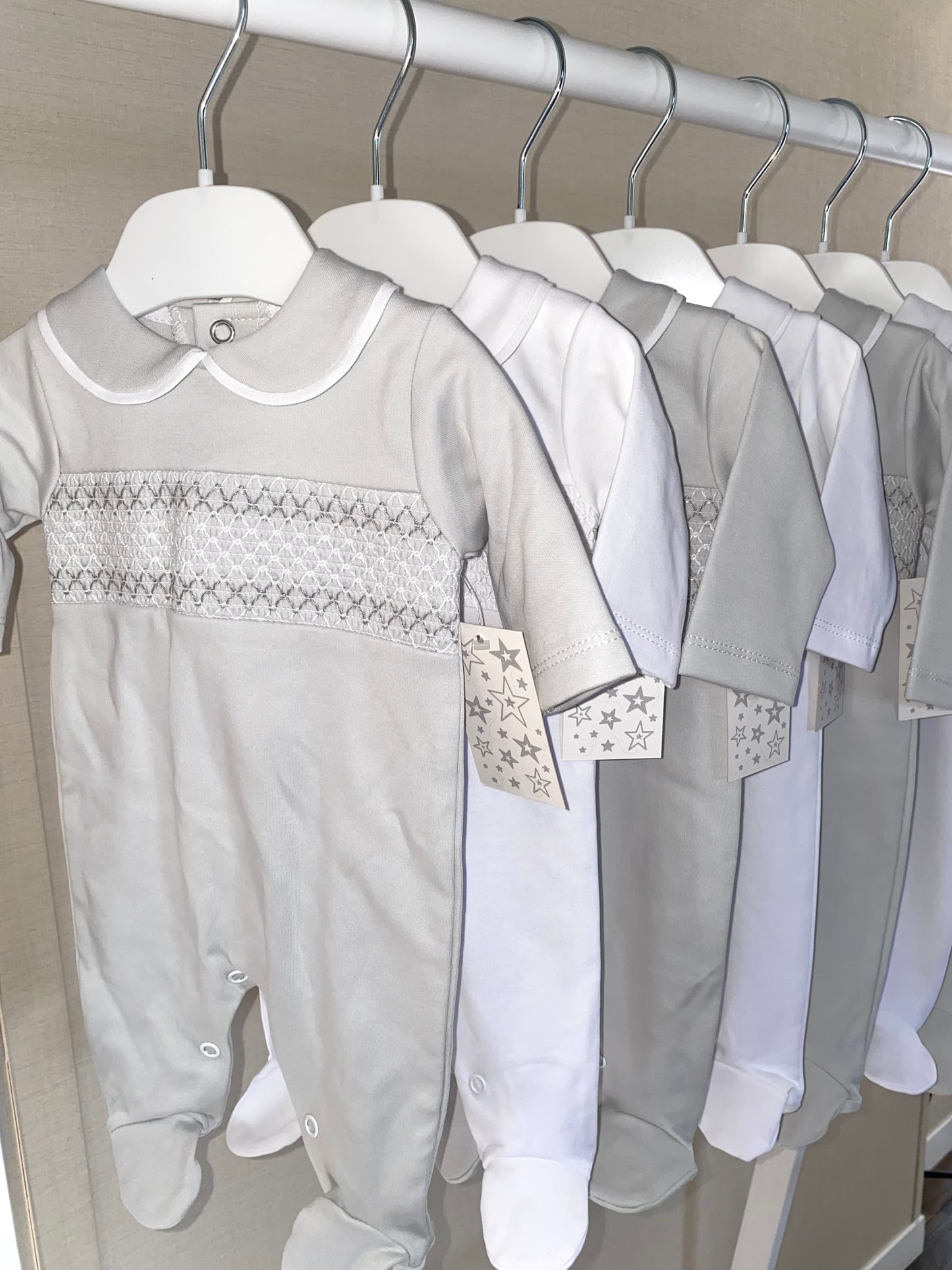 Row of baby outfits on hangers with a focus on a gray onesie.