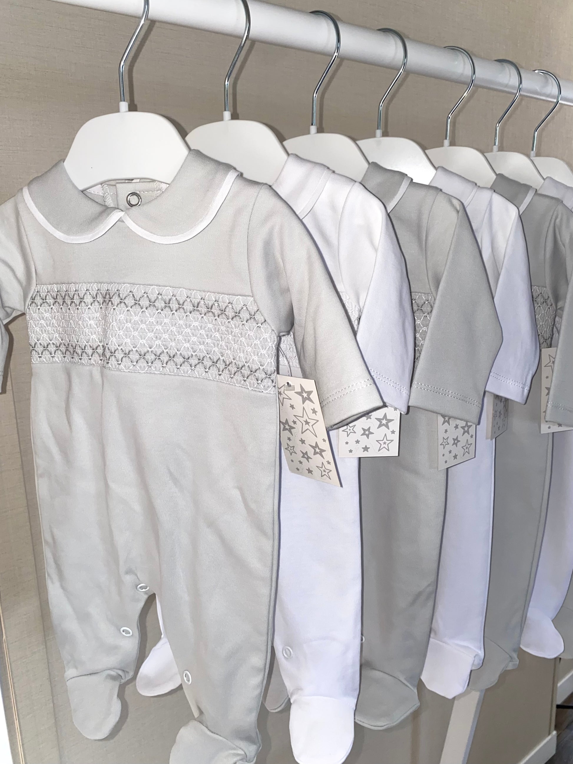 Row of baby outfits on hangers with a focus on a gray onesie.