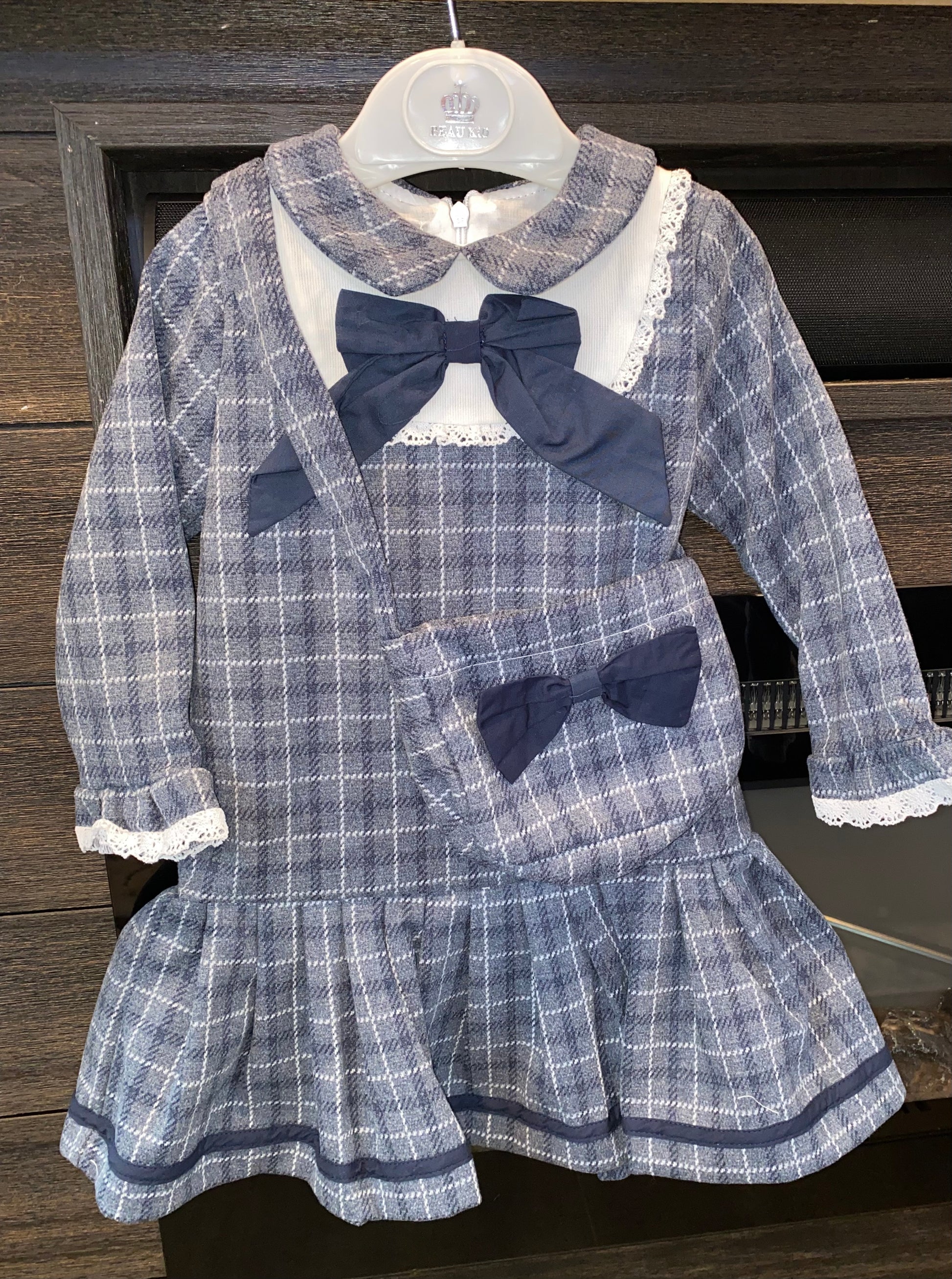 Children's blue plaid dress with bow details on a hanger against a wooden background