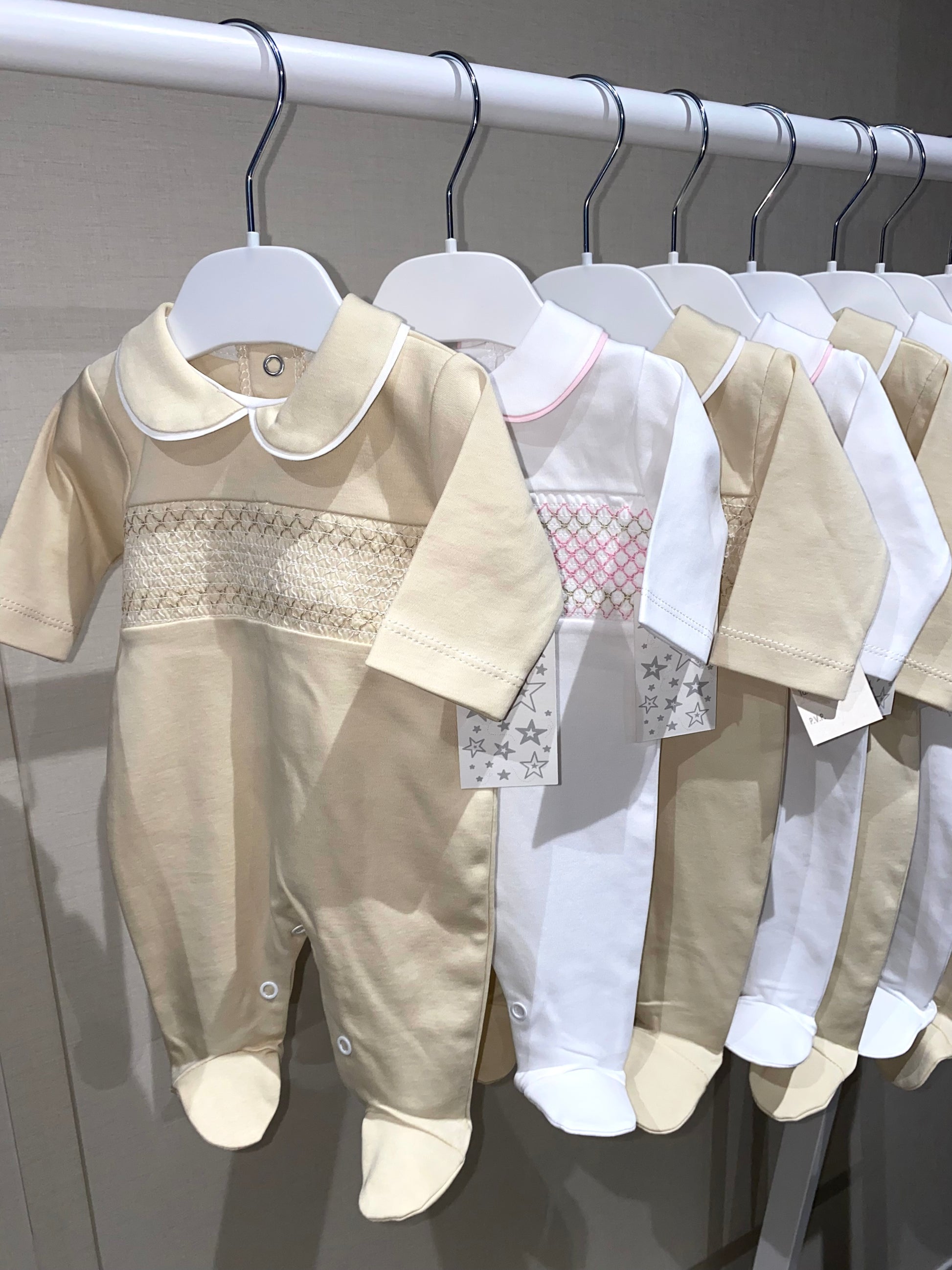 Row of spanish baby outfits on hangers against a neutral background