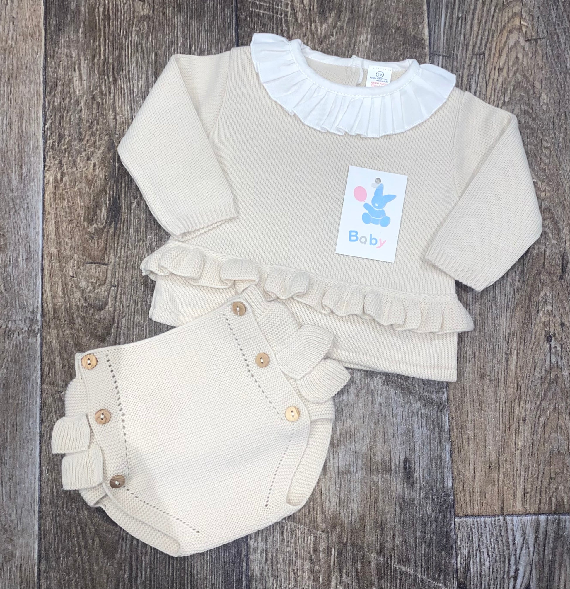 Baby outfit with sweater and bloomers on a wooden surface