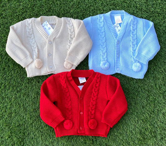 Three knit cardigans in beige, blue, and red on a grassy background