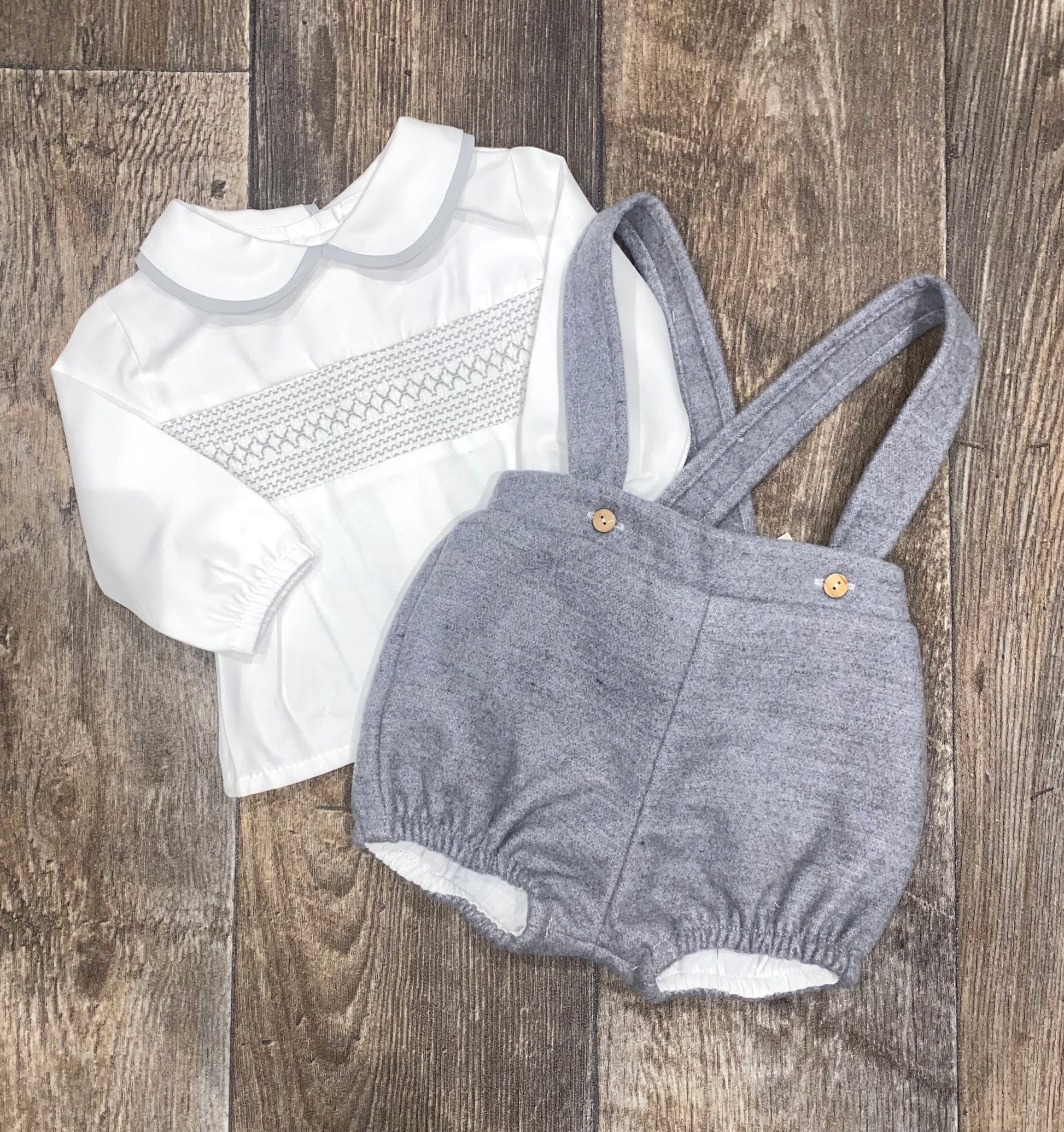 White shirt with smocking details and gray dungaree shorts on a wooden surface