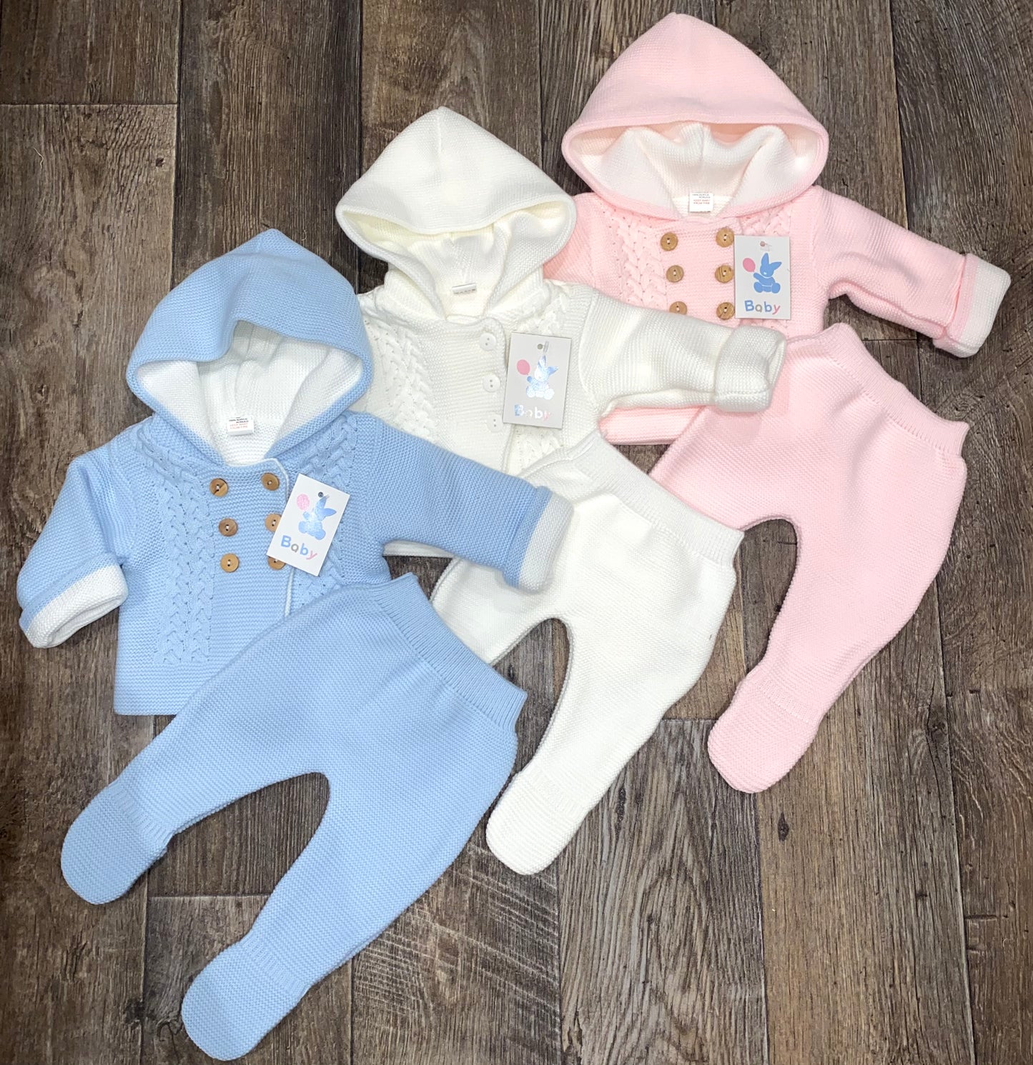 Three baby onesies in blue, white, and pink on a wooden surface.