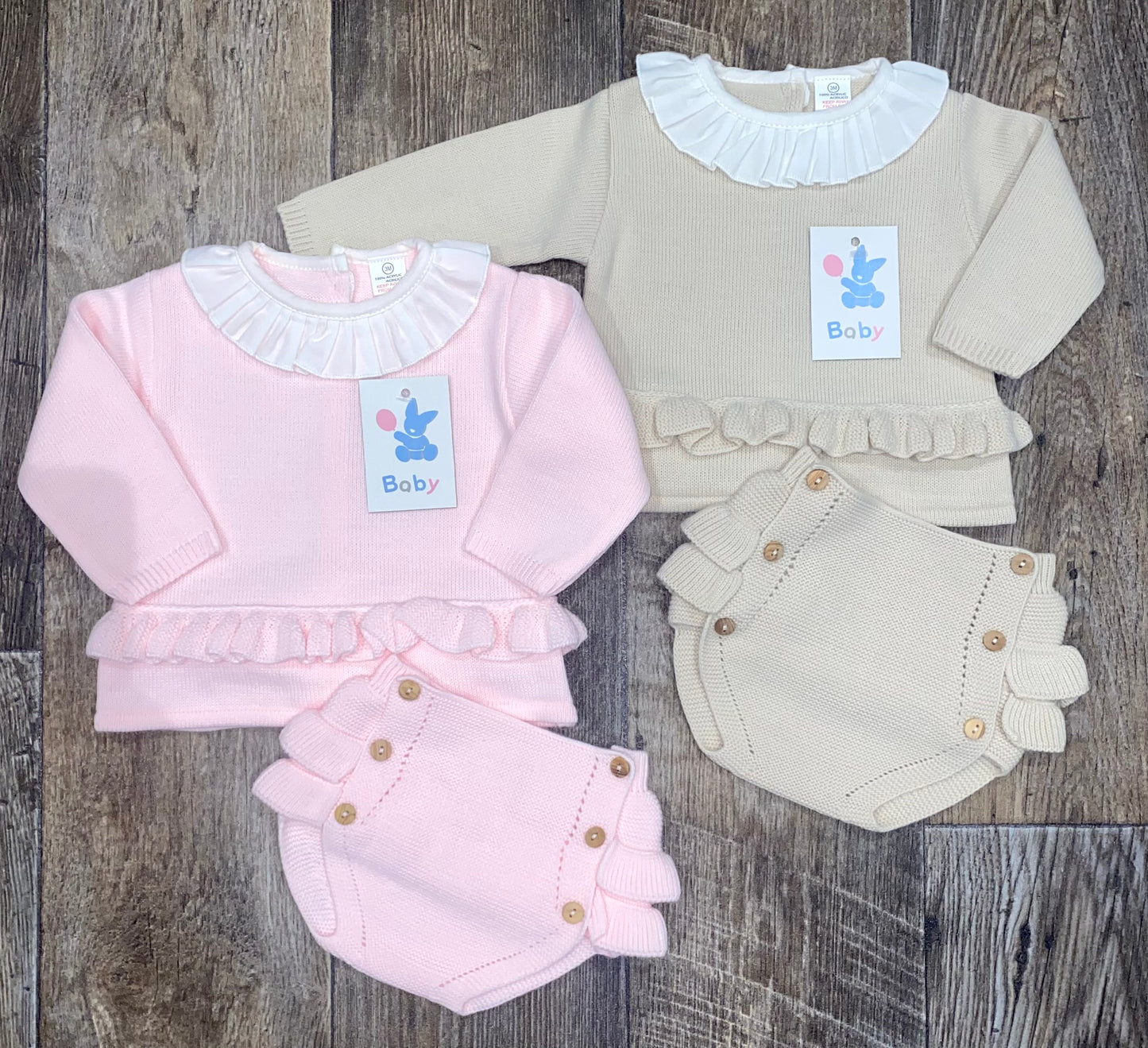 Two knitted baby outfits, one pink and one beige, on a wooden surface.