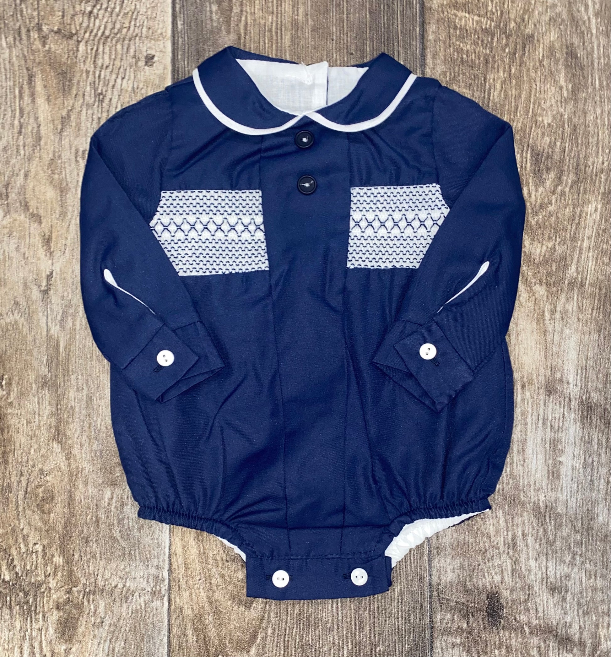 Navy blue baby romper with white patterns and buttons on a wooden surface