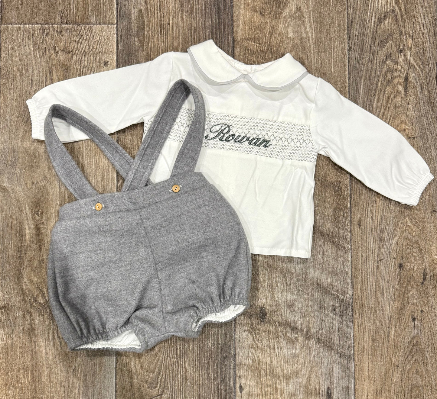 White long-sleeve shirt with embroidery name and gray shorts on a wooden surface