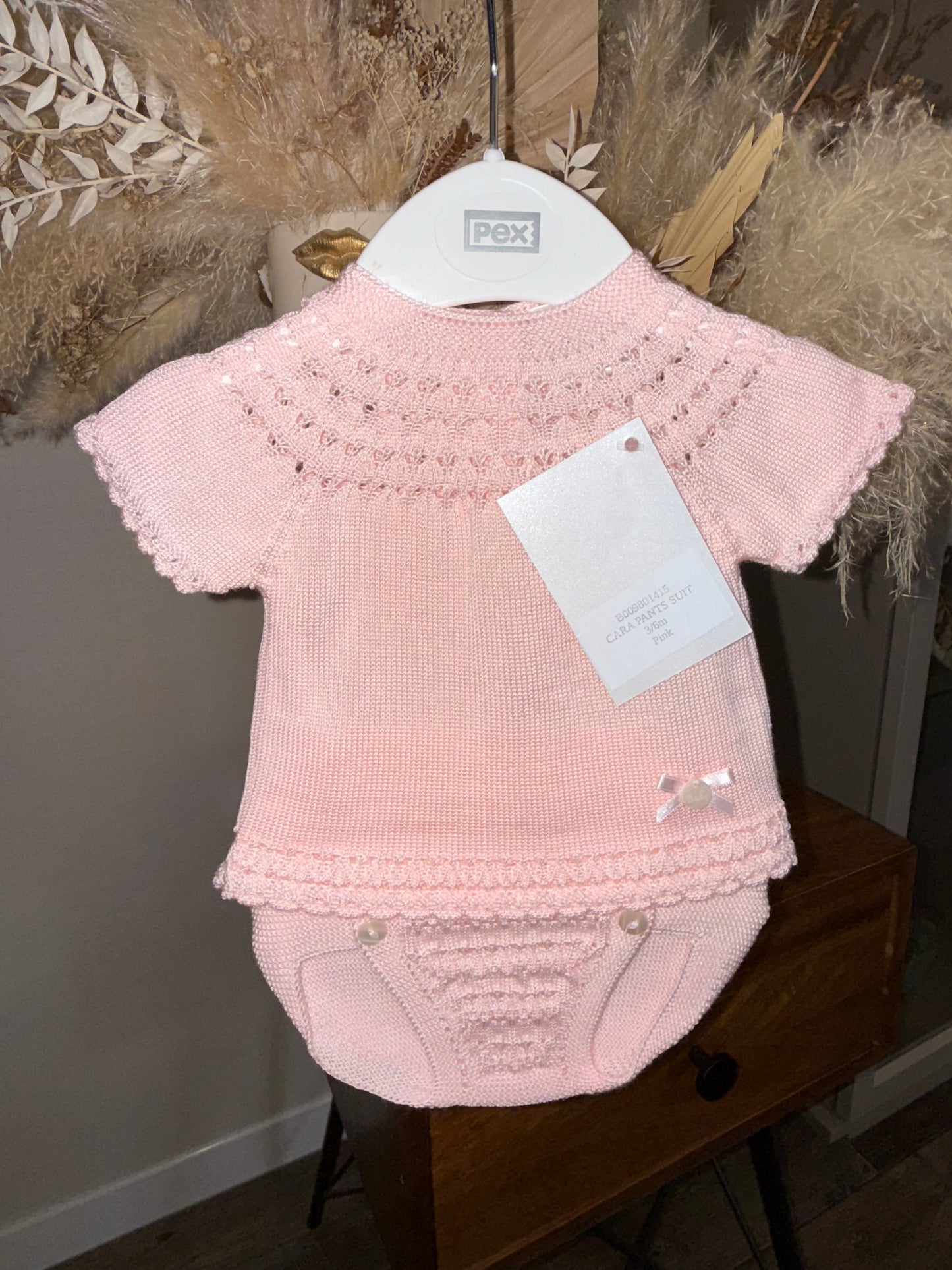 Pink knit baby outfit on a wooden surface