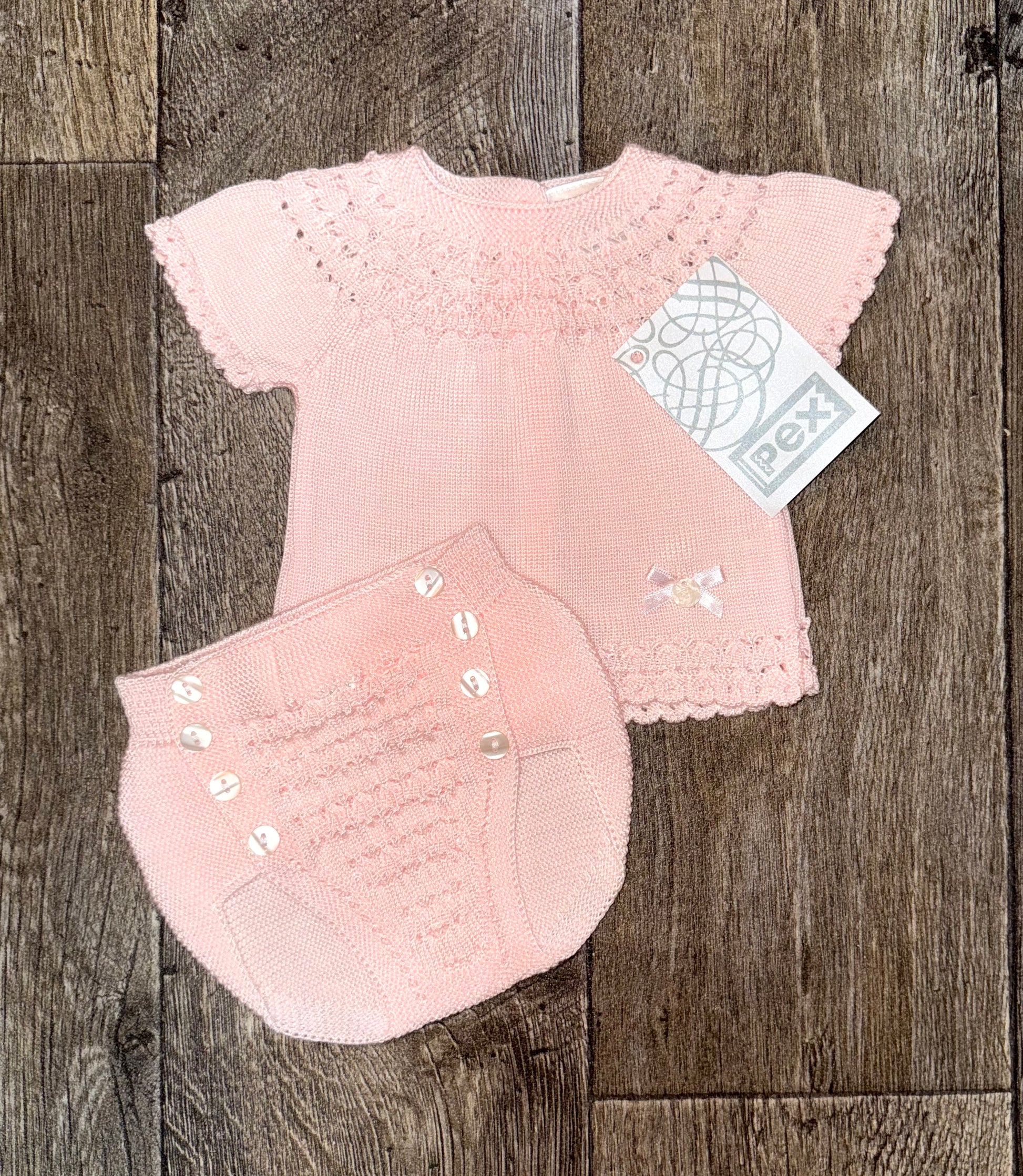 Pink baby outfit with matching knickers on a wooden surface.