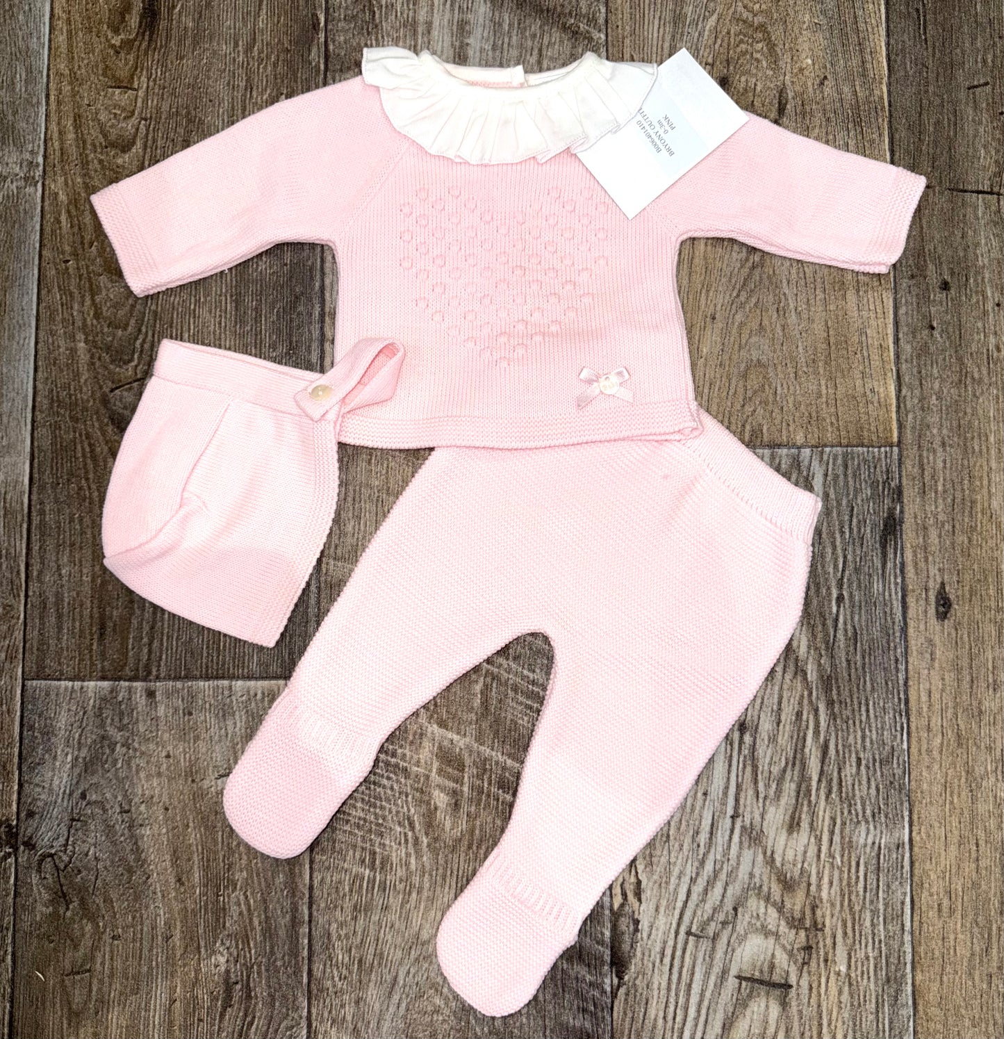 Pink baby outfit with matching hat on a wooden surface