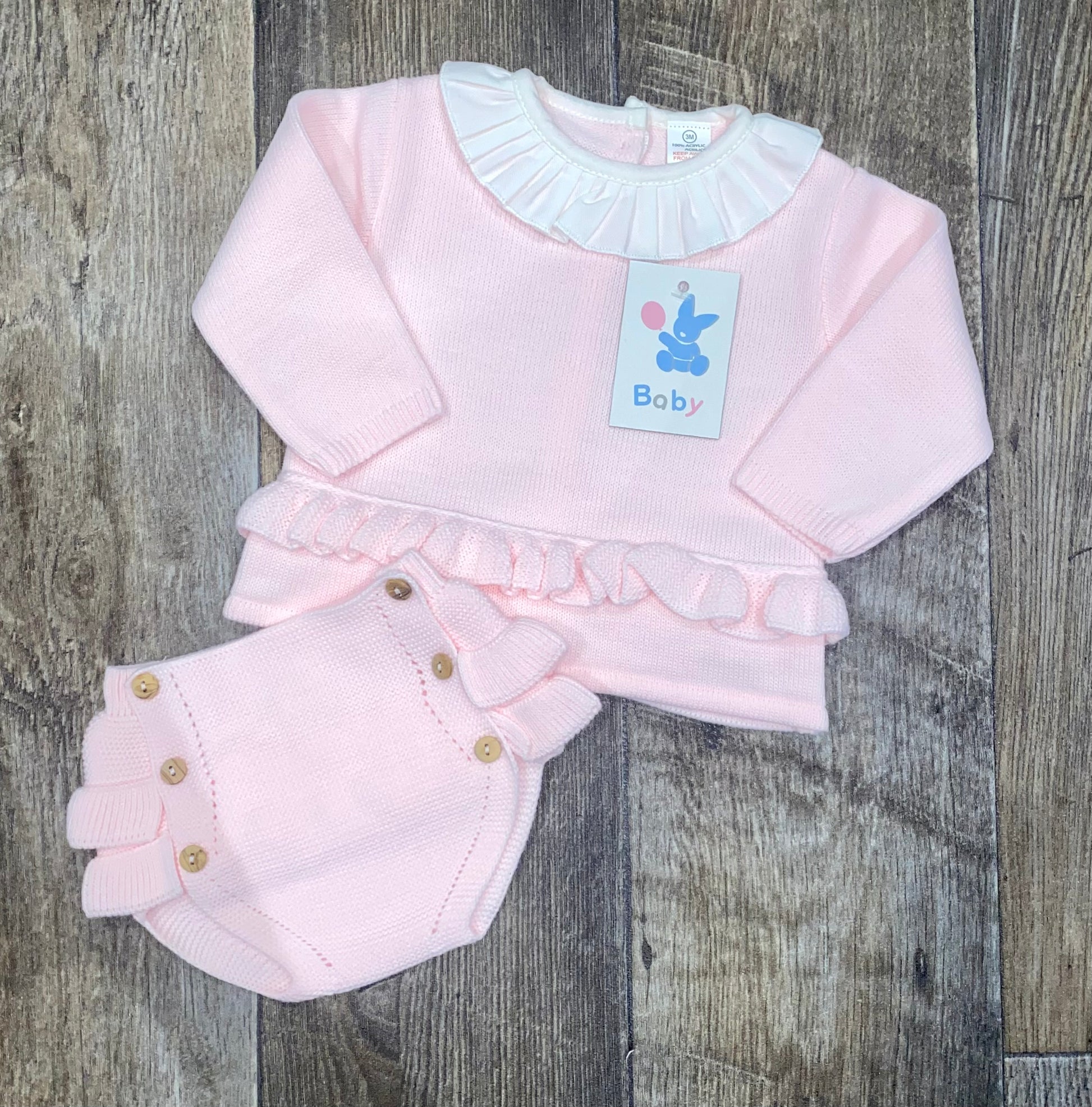 Pink knit baby outfit with ruffled details on a wooden surface