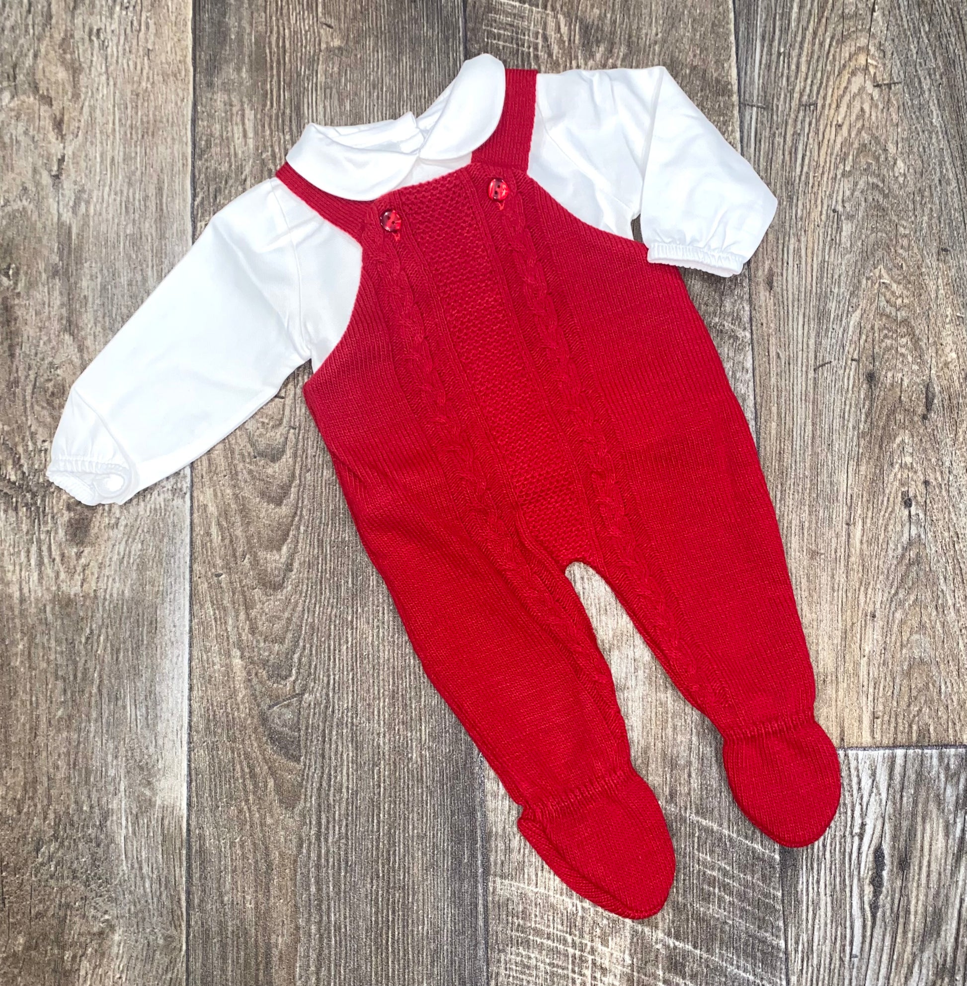 Red knitted baby romper with white shirt on a wooden surface