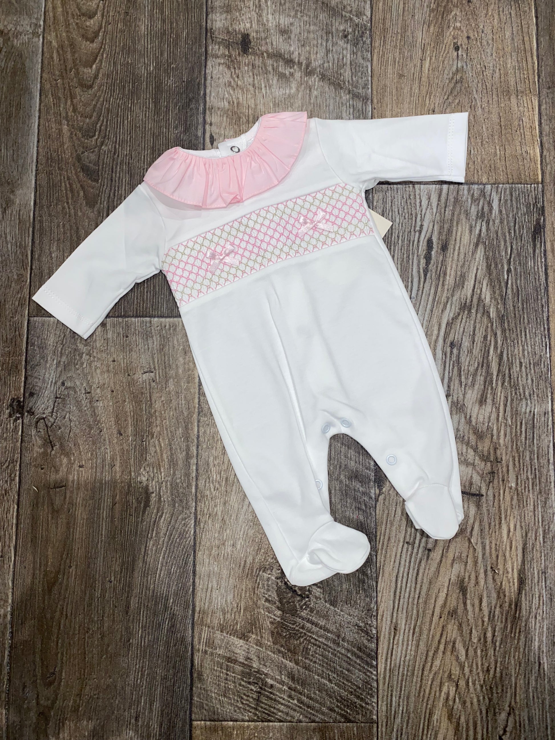 White smocking detail sleep suit with pink detail on a wooden surface