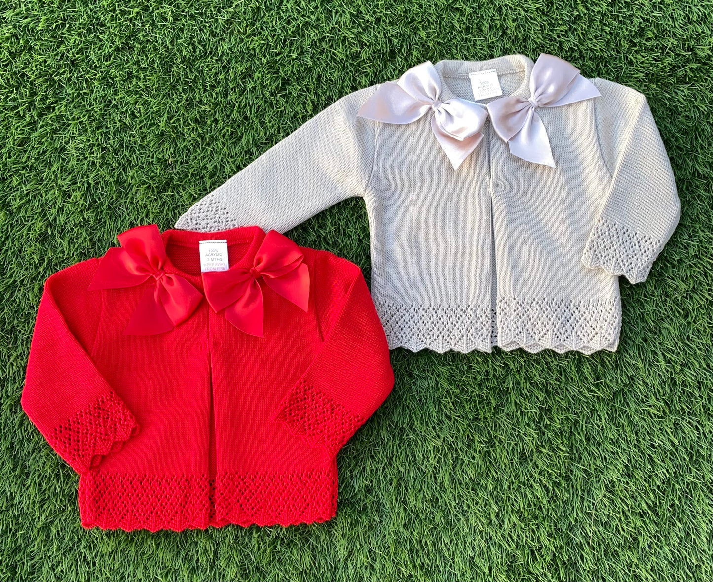 Red and taupe colour children's cardigans with lace details on a grass background