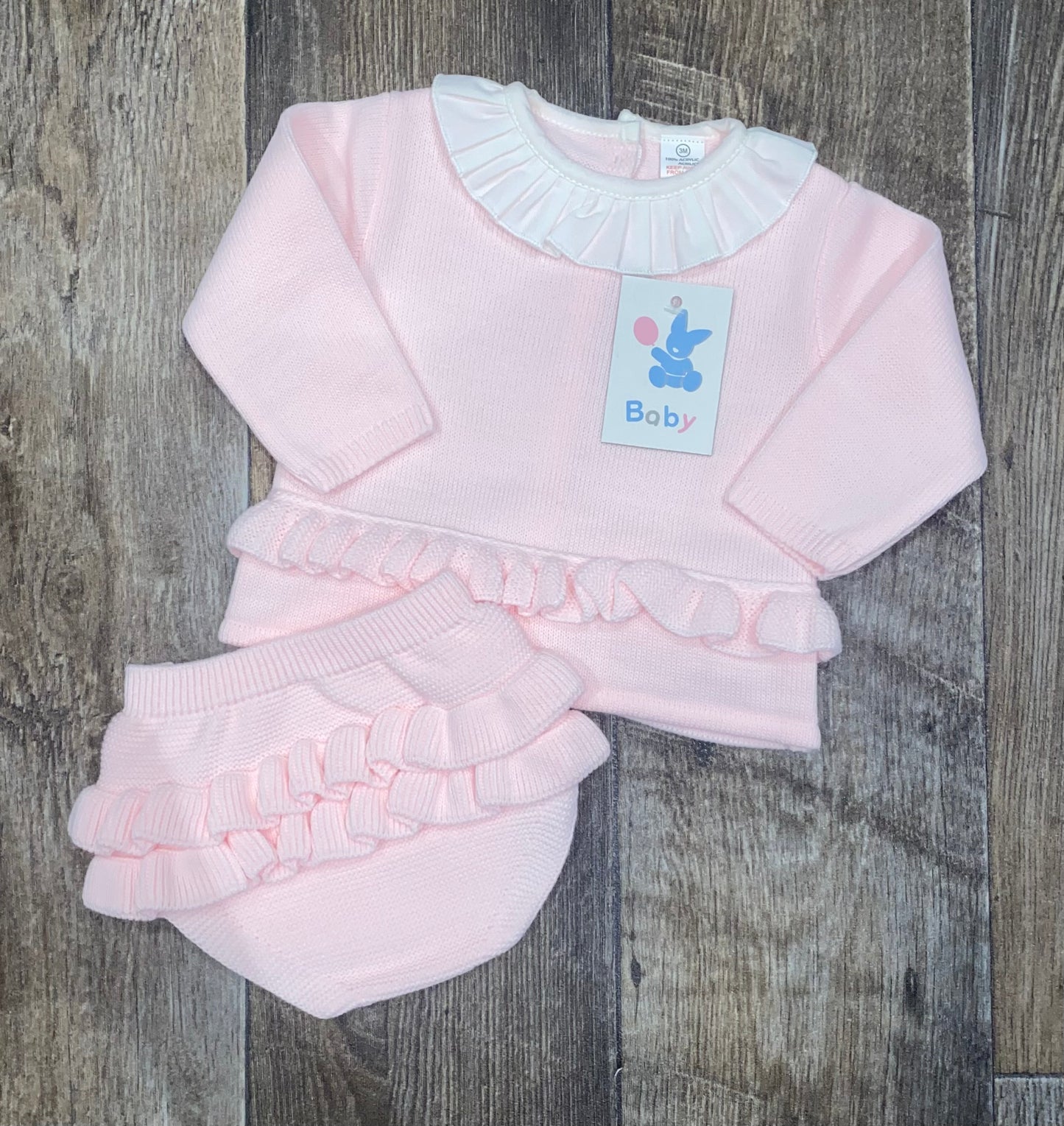 Pink baby outfit with ruffled details on a wooden surface